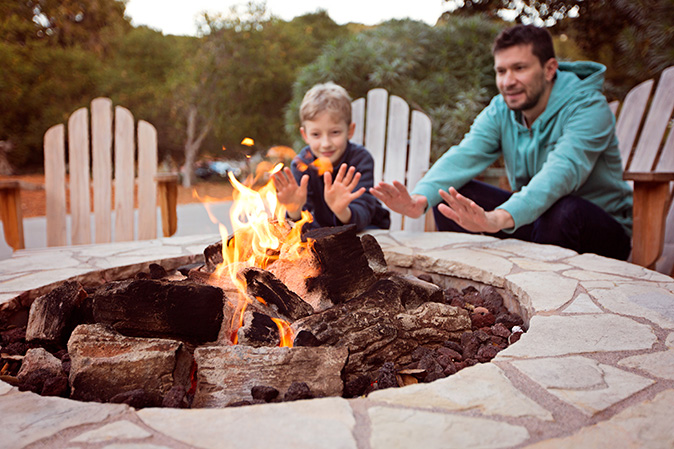 Family members warm their hands in front of a blazing wood fire in their stone fire pit.