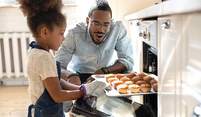 Father and daughter baking muffins in an oven