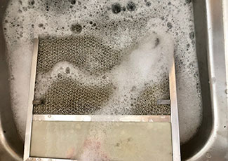 Cleaning dirty range hood filter in sink full of soapy water.
