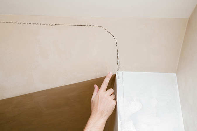 Person’s finger pointing at a cracked wall inside a house.