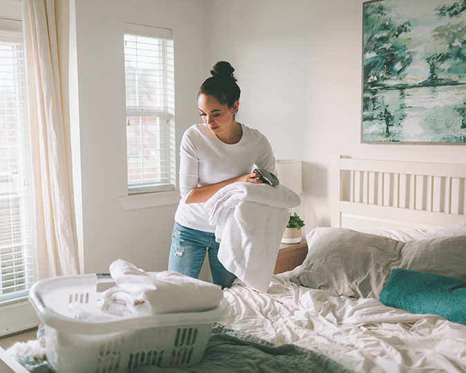 A woman folds laundry in a brightly lit bedroom.