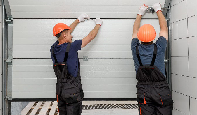 Two contractors in orange hard hats finishing a garage door replacement.