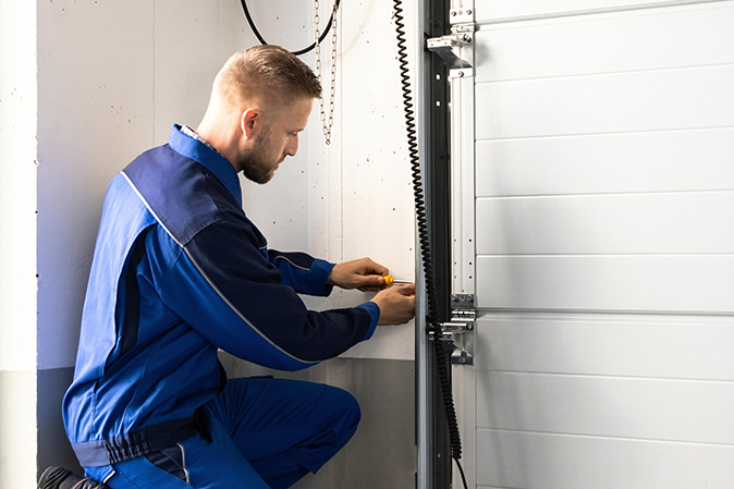 A contractor kneeling down and fixing a garage door opener.