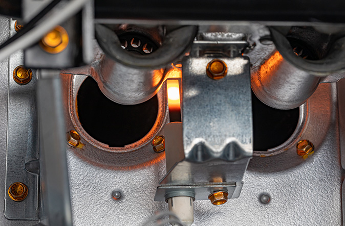 Closeup of gas furnace ignitor and flame sensor in a home’s heating system.