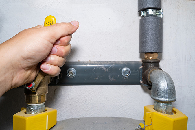 A person’s hand turning off a natural gas shutoff valve in the basement.