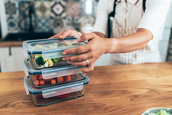 Person stacking up several glass food storage containers on wood table