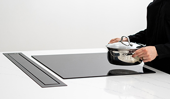 Image shows person setting pot on glass induction cooktop