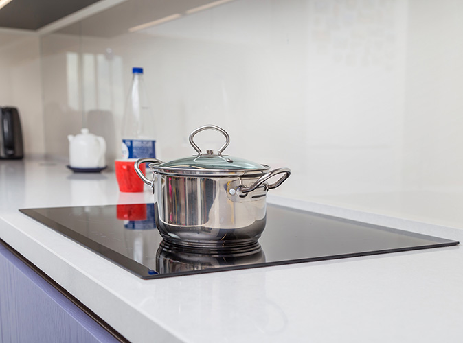 A stainless steel pot with a glass lid sits on a standalone electric cooktop.