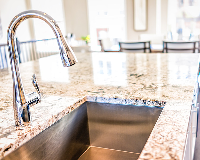New modern faucet and kitchen room sink closeup with island and granite countertops in model house, home, apartment.