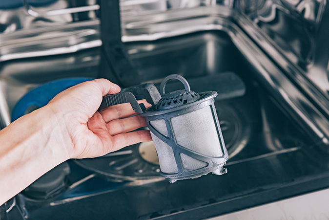A close-up of a person’s hand holding a dishwasher filter.
