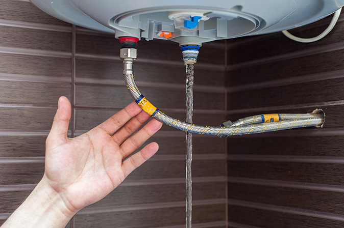 A person’s hand connecting a drain hose to a water heater.