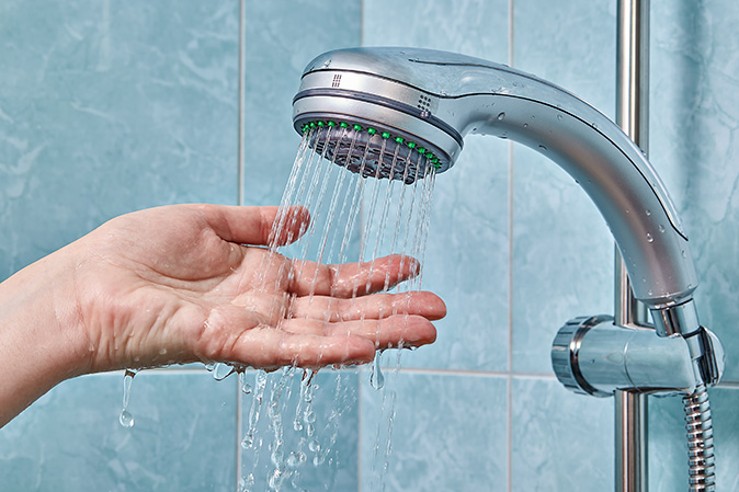 A close-up of a person’s hand under the running water of a showerhead.