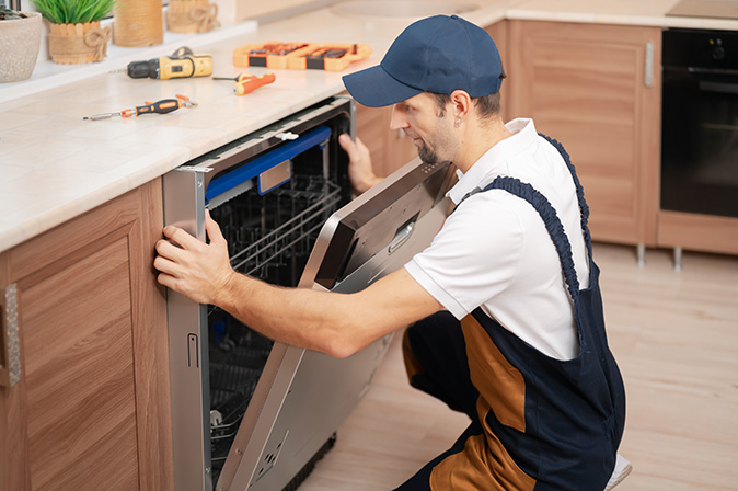 A handyman adjusting a dishwasher and pushing it into place.