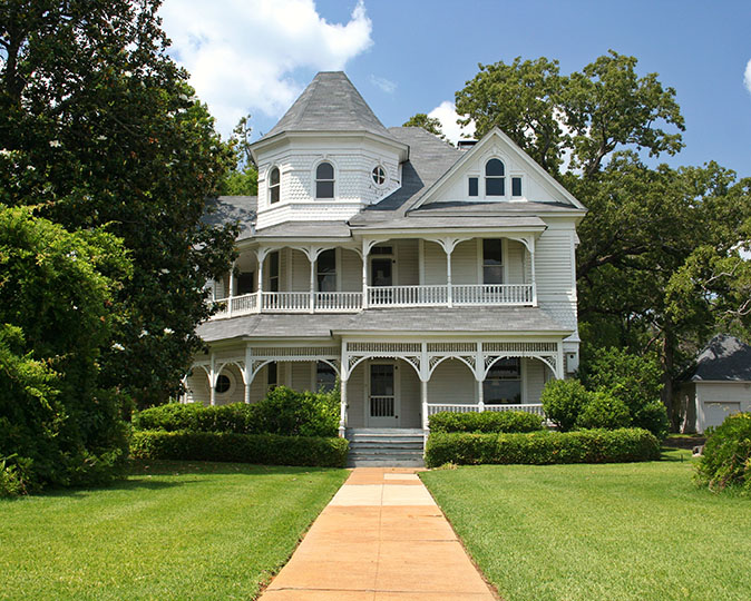 A view of a lush green lawn and path leading to a historic three-story Victorian home. 