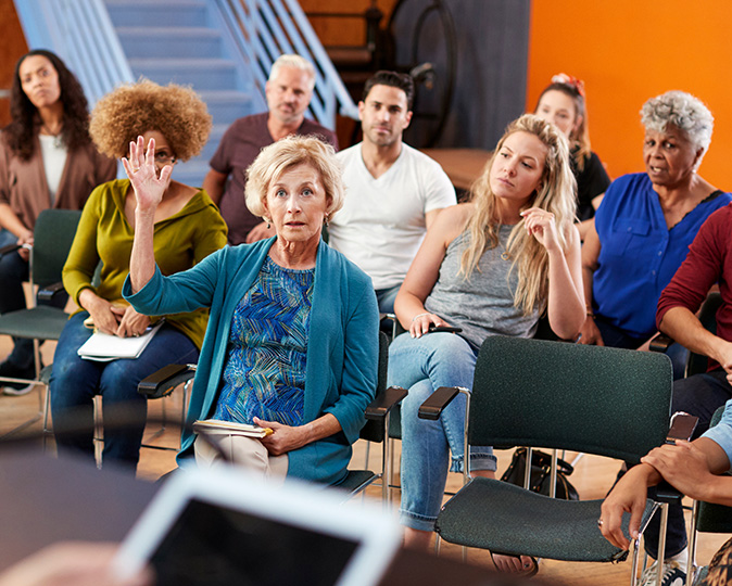 A homeowner raises her hand to speak at an HOA meeting.
