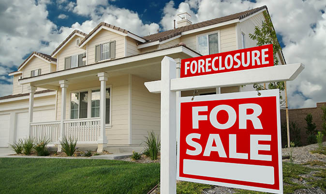 A well-kept two-story home with a hanging sign out front that says “foreclosure” and “for sale.”