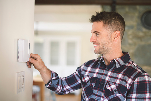 A homeowner in a flannel shirt turns down the thermostat when he gets home from work.