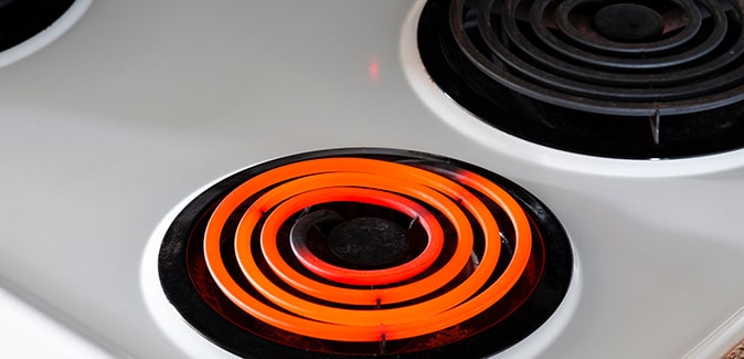 One burner on a white coil top electric stove lights up bright red with heat.