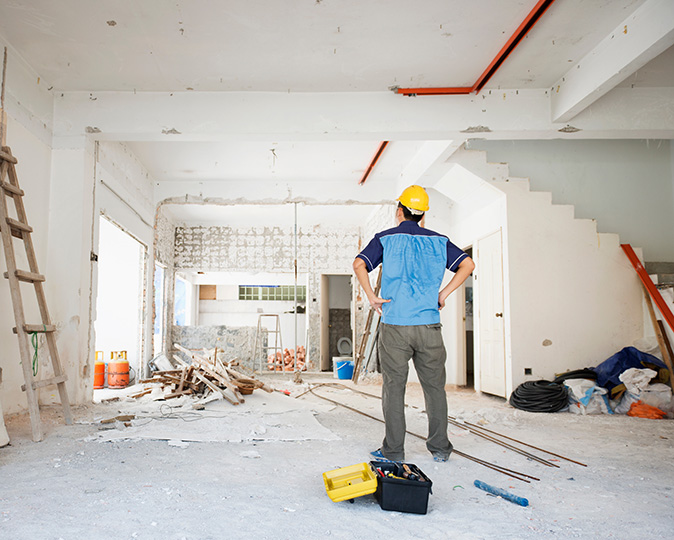 A contractor in a hard hat stands in the middle of a room under renovation.