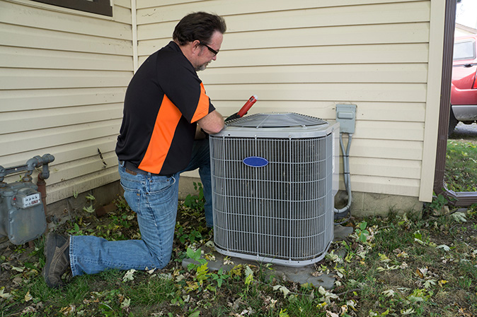 A repair technician checking out an HVAC system outside of a house.