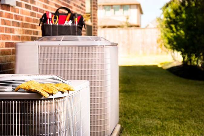 Work tools and gloves placed on top of outdoor air conditioner units against a brick home.