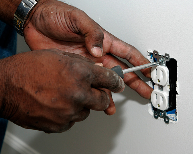 A man removes an outlet from the wall with a screwdriver.