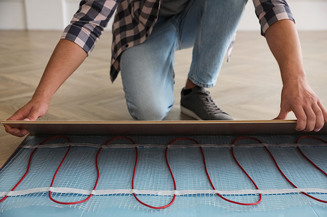 A male installer rolls out radiant heating mats before installing the flooring in a home.