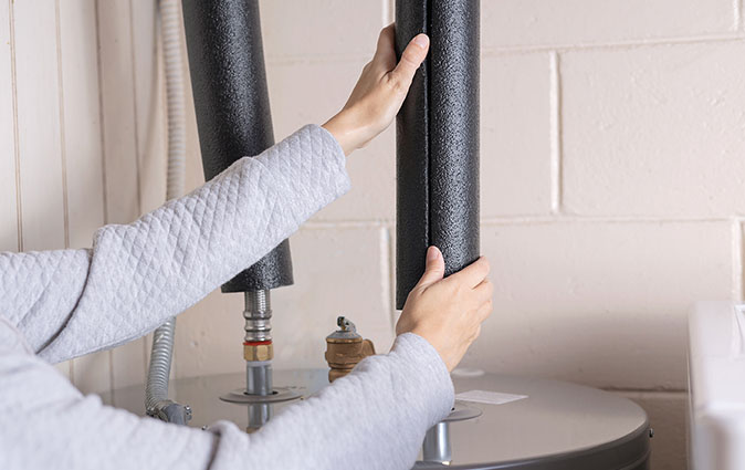 Person adding insulation to water heater pipes.