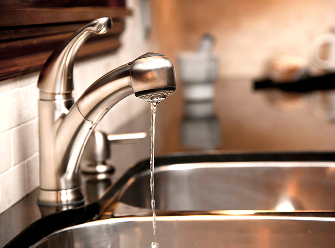 A disc faucet drips into a stainless steel sink. 