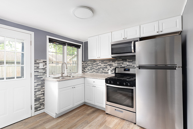 A bright, modern kitchen featuring a stainless-steel dishwasher, gas range, and vent hood.