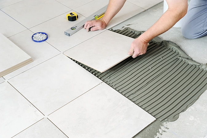 A person laying ceramic tiles on a bathroom floor.