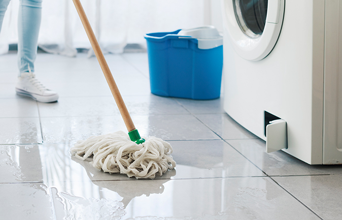 Homeowner uses a mop to absorb water on floor from leaking washing machine