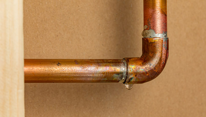 A copper pipe leaks water inside a home’s wall due to water pressure.