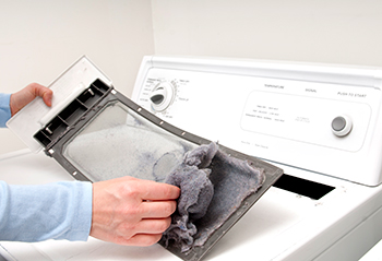 Adult male hand is removing lint from a dryer trap located at the top of the appliance