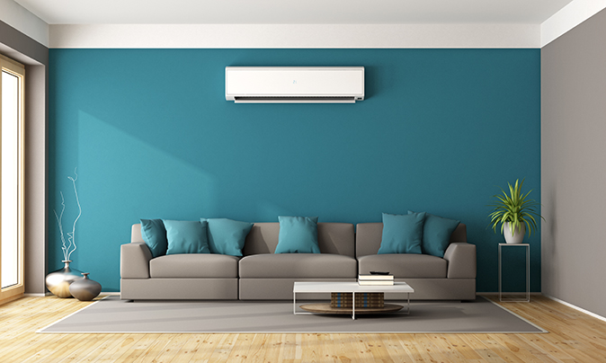 Ductless mini-split indoor air handler mounted on wall above a room with a blue couch.