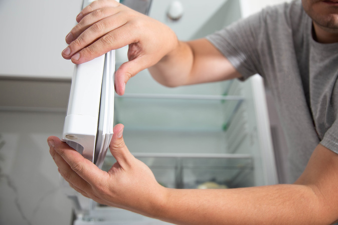 A person pushing down on a torn refrigerator door seal.