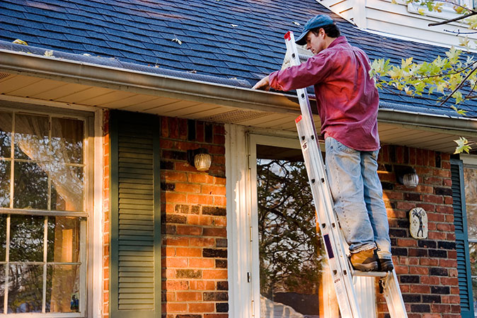 A man standing on a ladder cleaning out the gutters on a house.