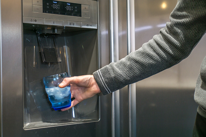A man filling a blue cup with water and ice from the dispenser on the refrigerator.