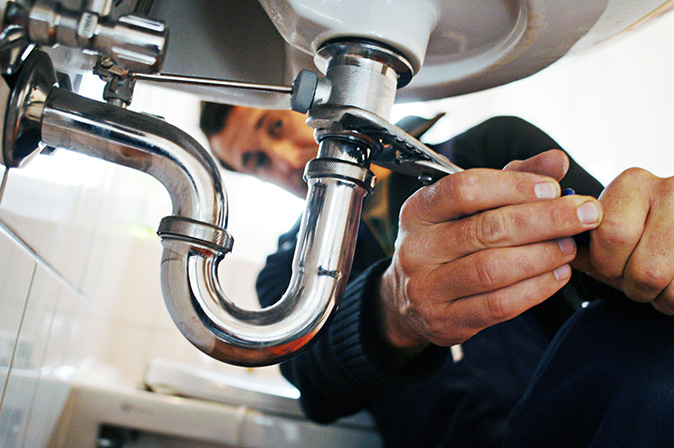 Homeowner is using a plumber's wrench to loosen the p-trap pipe under a sink.