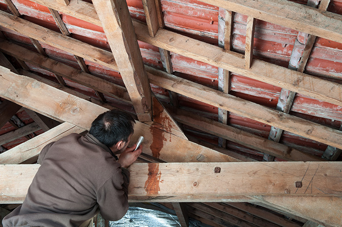 A man using a flashlight to inspect water dripping in the attic.