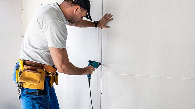 A homeowner finishes installing neat and well-fitted drywall with an electric screwdriver and drywall screws.