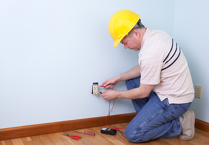 A man is testing a new GFCI outlet he installed in the wall of a home.