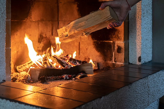 A man putting wood into his fireplace to keep it burning.