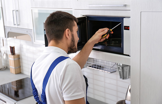A man repairing a microwave in a kitchen.