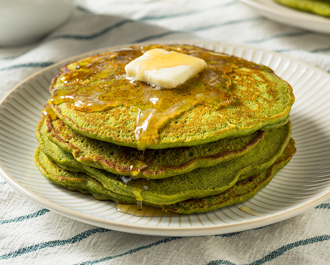 Festive green pancakes for St. Patrick’s Day sit on a white plate next to a suede leprechaun hat.