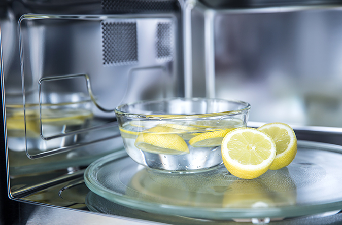 Image shows a bowl of water with lemons to be used for cleaning the inside of a microwave oven.