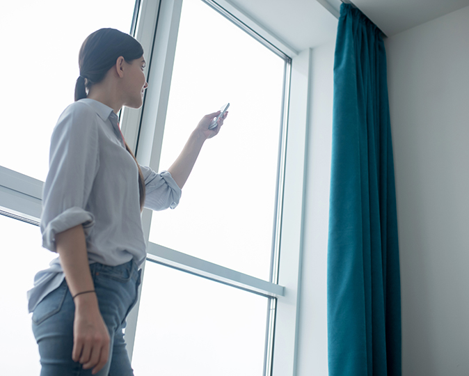 A homeowner adjusts her motorized blind with a phone app.