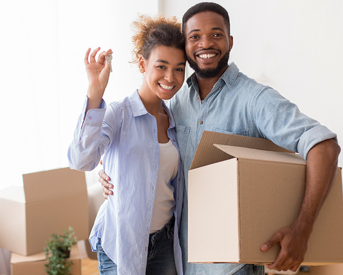 A young couple poses with the keys to their new home and moving boxes.