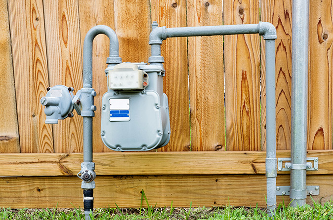 A residential natural gas meter in a yard with a wooden fence in the background.