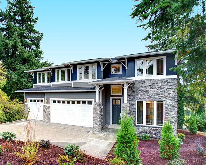 A newer model home surrounded by pine trees features partial stone veneer siding.